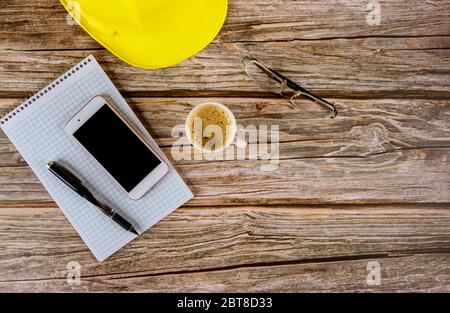 Work architect space builders office construction, using spiral notepad book on yellow hard hat with pen and cup of coffee, smartphone eyeglasses Stock Photo