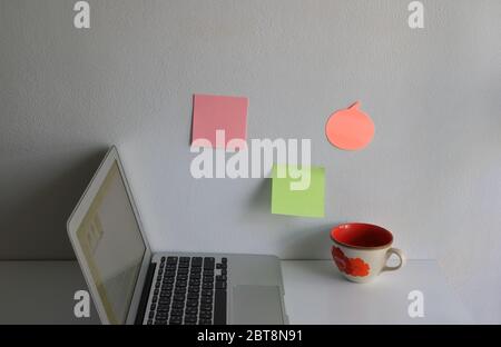 Closeup and selective focus on blank sticky notes attached to the wall at workplace with notebook and a cup on wooden table Stock Photo