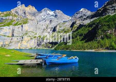 Popular hiking and leisure place with lake Oeschinensee. Moored recreation boats and high mountains with glaciers in background, Bernese Oberland, Swi Stock Photo