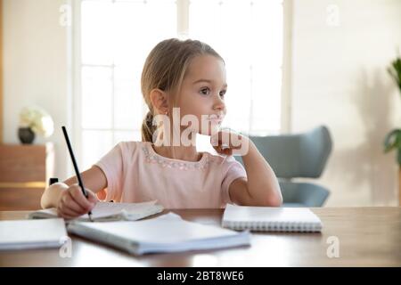 Smiling little girl dreaming distracted from studying Stock Photo