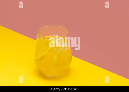 Immune-boosting iced lemon ginger turmeric tea in a glass cup on pink and yellow background with space for text Stock Photo