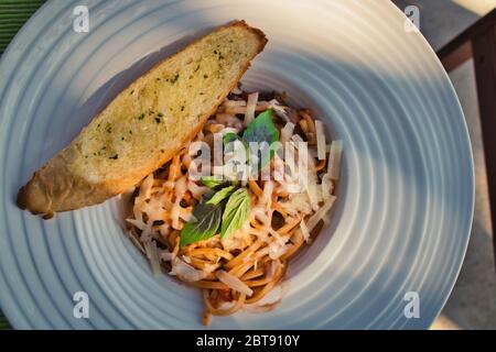 This unique photo shows the Italian meal spaghetti bolognese. Served in a deep plate with garlic baguette and a basil leaf as decoration. Stock Photo