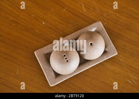 This unique photo shows a salt and pepper shaker made of stone from above in a bowl on a brown wooden table. The picture was taken in Thailand Stock Photo