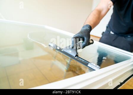 A professional cleaner using a squeegee and scraper to clean a large apartment window Stock Photo