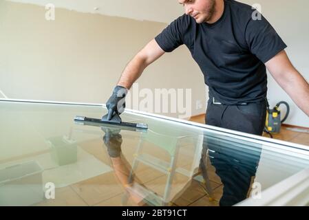 A professional cleaner using a squeegee and scraper to clean a large apartment window Stock Photo