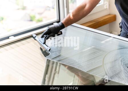 A professional cleaner using a squeegee and scraper to clean a large apartment window Stock Photo