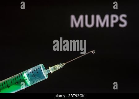 This photo illustration shows a disposable syringe with hypodermic needle, MUMPS written on a black board behind Stock Photo
