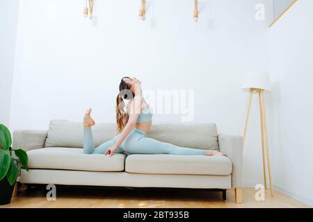 She drop into the splits, on the couch, doing daily stretching Stock Photo