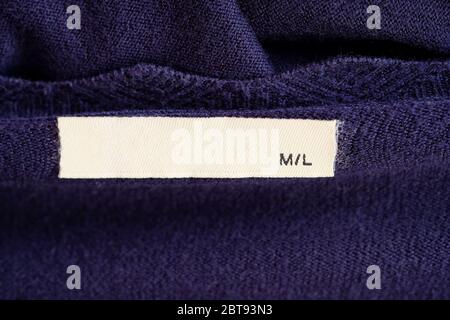 Clothes label on purple textile background closeup. Blank white clothes label on knitted sweater. Cloth label  blank mockup rectangular on a collar wi Stock Photo