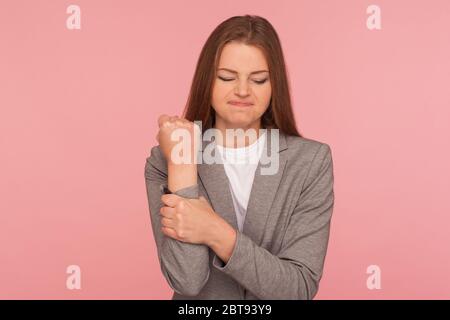 Injured hand, trauma. Portrait of unhealthy young woman in business suit feeling pain in wrist and grimacing, suffering carpal tunnel syndrome, pinche Stock Photo