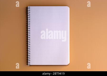Notebook with spring and sheets in a cage top view. Blank paper in a notebook on a beige background. Stationery, notebook for notes. Copy space. Stock Photo