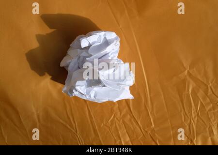 Crumpled white paper on a gold background. Rolled paper on a crumpled brown background, paper shadow. Concept of bad ideas, finding solutions, outline Stock Photo