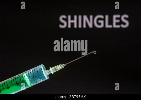 This photo illustration shows a disposable syringe with hypodermic needle, SHINGLES written on a black board behind Stock Photo