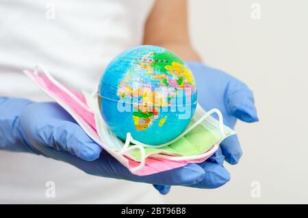 Hands covered with surgical gloves holding earth  globe and face masks representing the concept of protecting  population against disease transmission