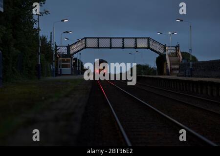 Northern Rail class 156 sprinter train departing from  Kirkby In Furness railway station on the Cumbrian coast railway line at dusk Stock Photo