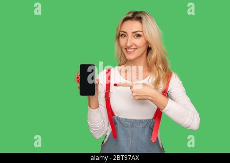 Look at cell phone, great app! Portrait of happy adult woman pointing to smartphone with mock up display, copy space for advertising application or we Stock Photo