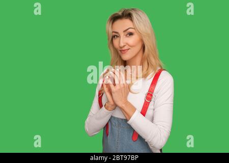 Portrait of sneaky scheming beautiful adult woman in stylish overalls pondering revenge and smiling slyly, thinking over devious plan, having cunning Stock Photo