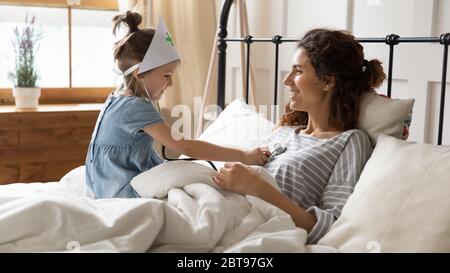 Cute little girl playing doctor with mother, using stethoscope Stock Photo