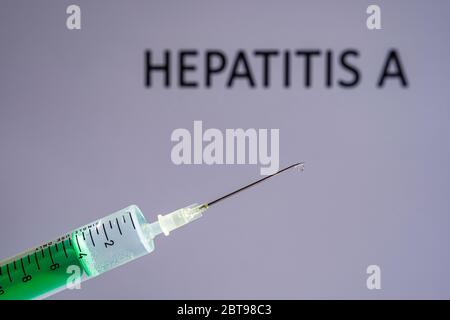 This photo illustration shows a disposable syringe with hypodermic needle, HEPATITIS A written on a grey board behind Stock Photo