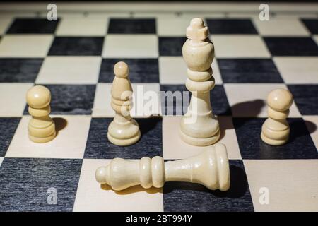 White queen fallen on the chessboard and behind her the king and other pieces Stock Photo
