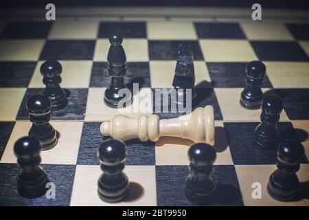 White queen fallen on the chessboard and around the black pieces Stock Photo