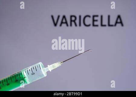 This photo illustration shows a disposable syringe with hypodermic needle, VARICELLA written on a grey board behind Stock Photo