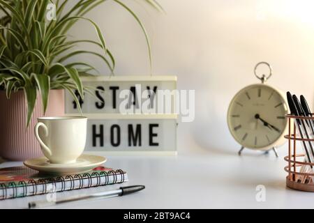 Home office desc concept during self quarantine as preventive measure against virus. Stay safe concept. Cup of coffee, clock, stationary, home plant on white background Stock Photo