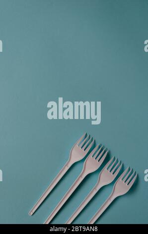 Four white plastic forks with shadows on a light blue background. Creative background using disposable cutlery. Place for text. View from above. Stock Photo