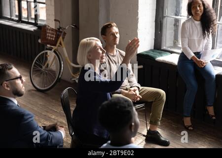 Middle aged businesswoman raising hand, asking question at briefing Stock Photo