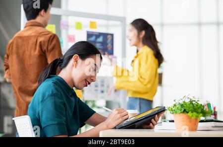 asian ux developer and ui designer using tablet testing mobile app interface design with colleagues at whiteboard in meeting at modern office.Creative Stock Photo