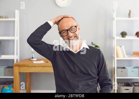 A man is looking at the camera online. Happy aged man smiling holds his head with his hand looks at the camera records video at home. A middle-aged bu Stock Photo