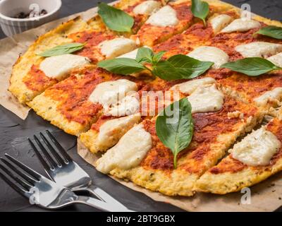 sliced homemade cauliflower pizza crust with mozarella and fresh basil in dripping pan on black concrete background. Stock Photo