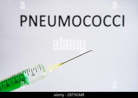 This photo illustration shows a disposable syringe with hypodermic needle, PNEUMOCOCCI written on a white board behind Stock Photo