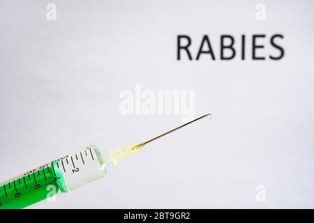 This photo illustration shows a disposable syringe with hypodermic needle, RABIES written on a white board behind Stock Photo