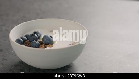 ripe blueberries and chocolate granola in white bowl on terrazzo surface Stock Photo