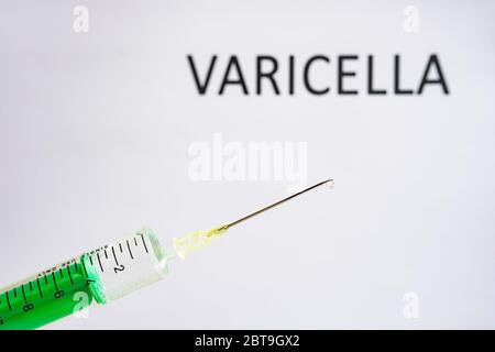 This photo illustration shows a disposable syringe with hypodermic needle, VARICELLA written on a white board behind Stock Photo