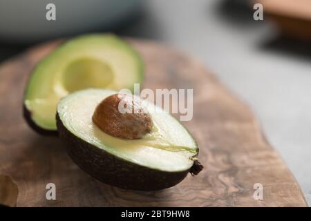 Ripe avocado sliced in halves on olive wood board closeup Stock Photo