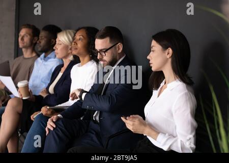 Diverse candidates waiting for job interview, sitting in row Stock Photo
