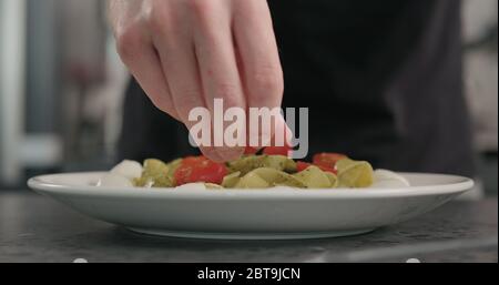 man put cherry tomatoes on pesto fettuccine with mozzarella in pasta bowl on concrete countertop Stock Photo