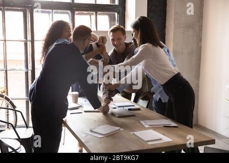 Excited diverse business people stacking fists at table, team building Stock Photo