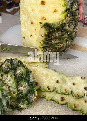Large knife peeling whole pineapple on the desk in a kitchen Stock Photo