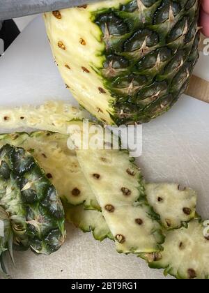 Large knife peeling whole pineapple on the desk in a kitchen Stock Photo