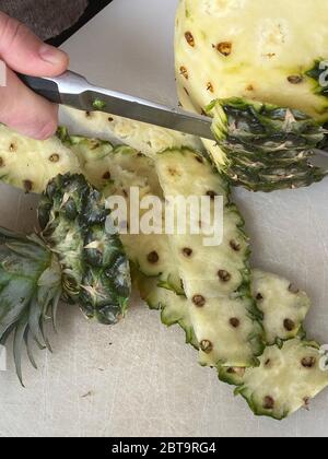 Large knife peeling whole pineapple on the desk in a kitchen Stock Photo