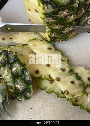 Large knife peeling whole pineapple on the desk in a kitchen Stock Photo