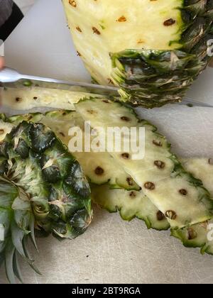 Large knife peeling whole pineapple on the desk in a kitchen Stock Photo