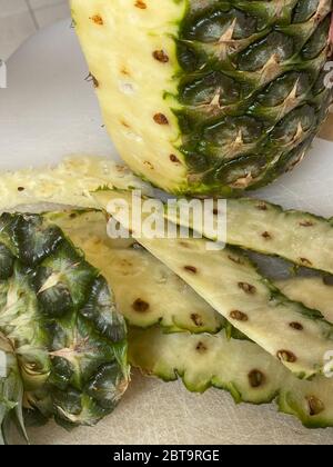 Large knife peeling whole pineapple on the desk in a kitchen Stock Photo