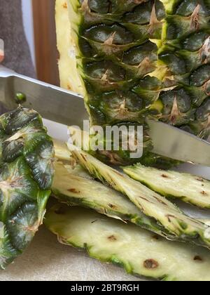 Large knife peeling whole pineapple on the desk in a kitchen Stock Photo