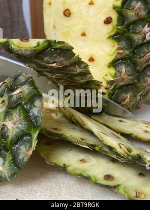 Large knife peeling whole pineapple on the desk in a kitchen Stock Photo