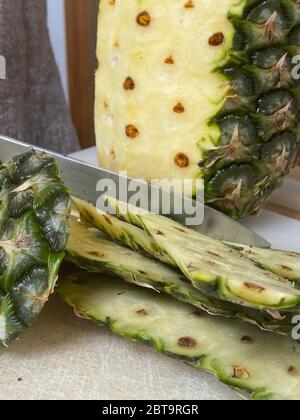 Large knife peeling whole pineapple on the desk in a kitchen Stock Photo