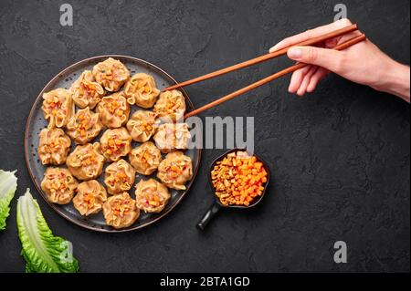 Shumai or Kanom Jeeb or Steamed Pork and Shrimp Dumplings on a black plate on dark slate backdrop. Shumai is a chinese cuisine dish with minced pork m Stock Photo